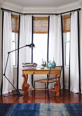 This is a good look for a bay window. Dress curtains edged in black, ties in with the black lamp and chair frame, and softens the wooden blinds